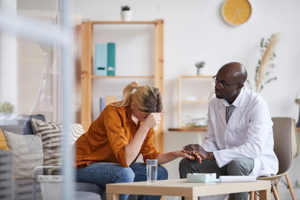 distressed woman on a couch holds therapist's hand during counselling session