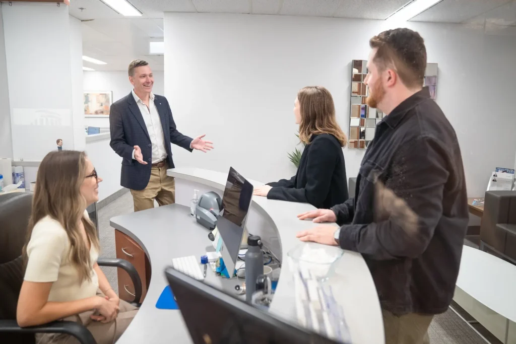 Mike Dull, a lawyer, smiles while conversing with a man and woman at his desk, creating a welcoming atmosphere.