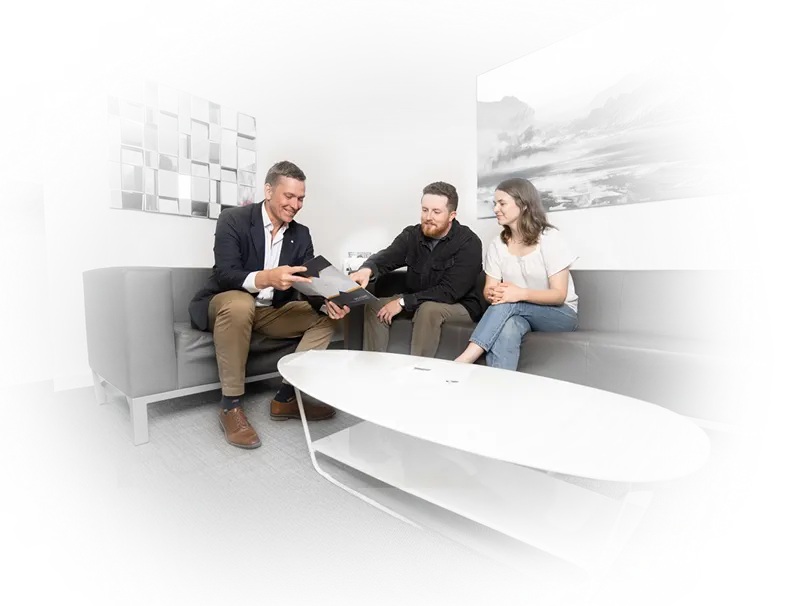 Mike with other two people sitting on a couch, talking and looking at papers held by Mike