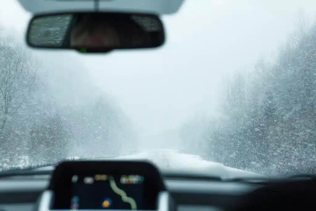 A view on the winter wood and mountains covered with the snow from windshield of the car.