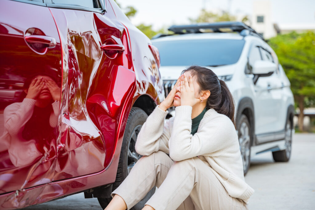 person sitting on the road next to their car after accident
