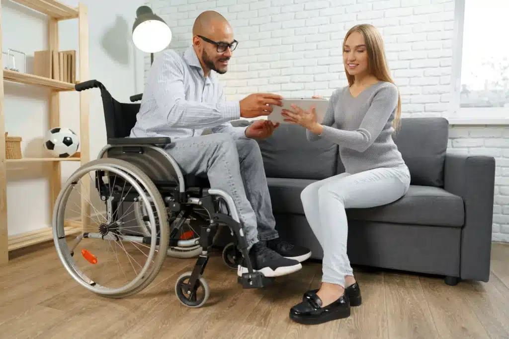 Disabled man in wheelchair and his pregnant caucasian wife watch something on digital tablet