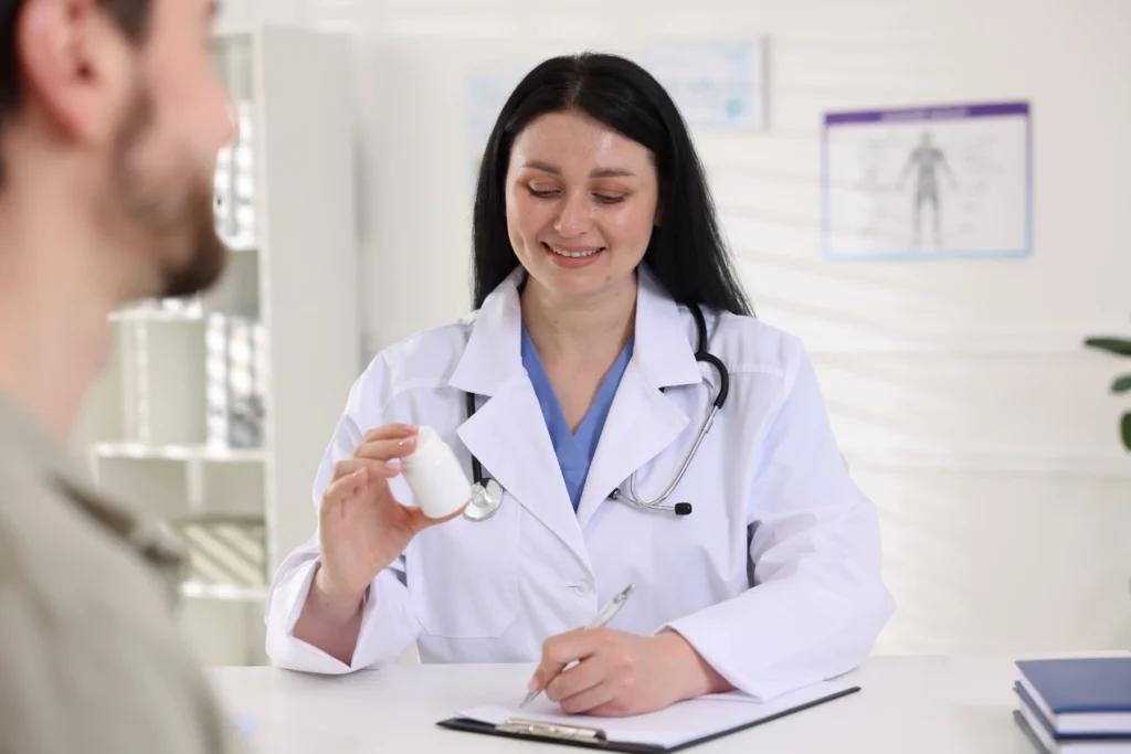 Doctor with bottle of pills consulting patient at table in hospital