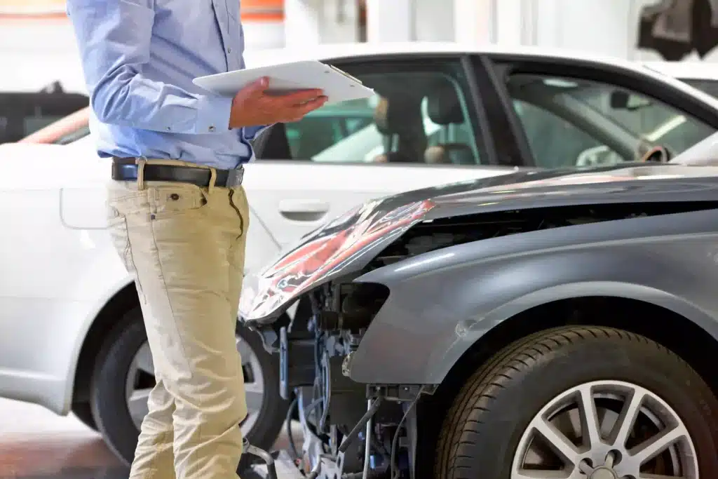 Insurance Assessor With A Clipboard Inspecting A Damaged Vehicle At The Garage.
