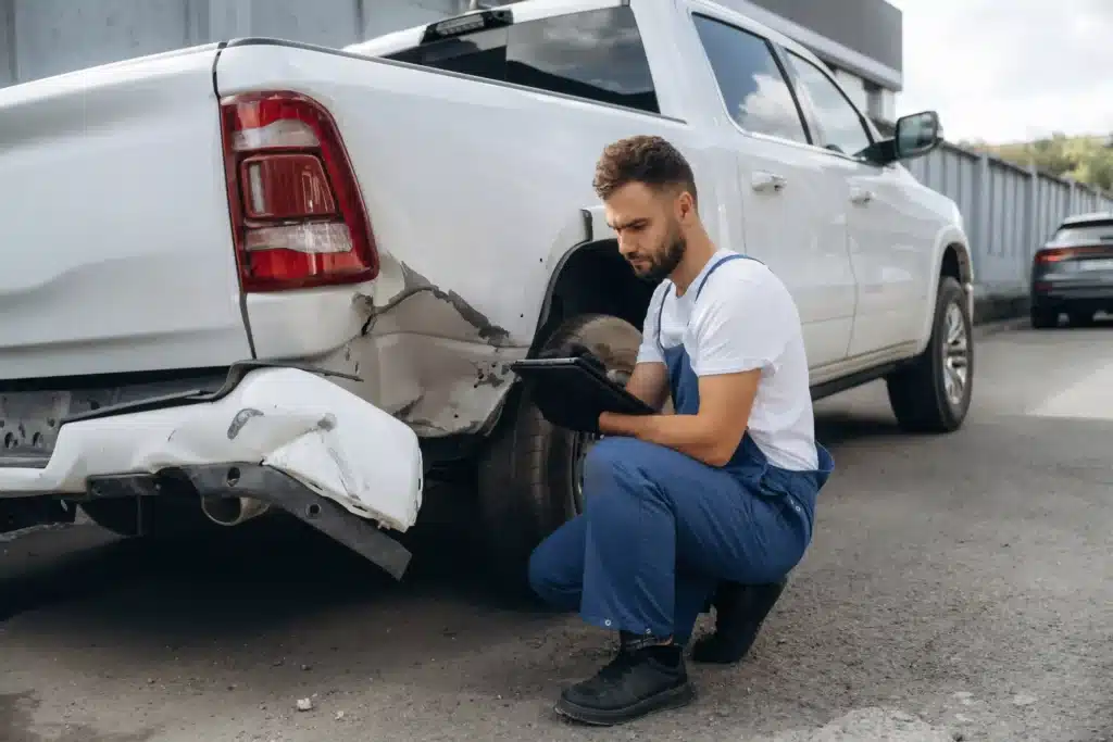 Mechanic is sitting by the damaged pickup truck outdoors