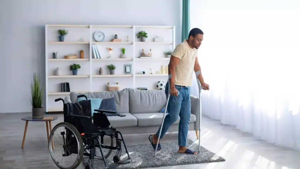 "Rehabilitation concept. Young black guy walking with crutches after using wheelchair at home "