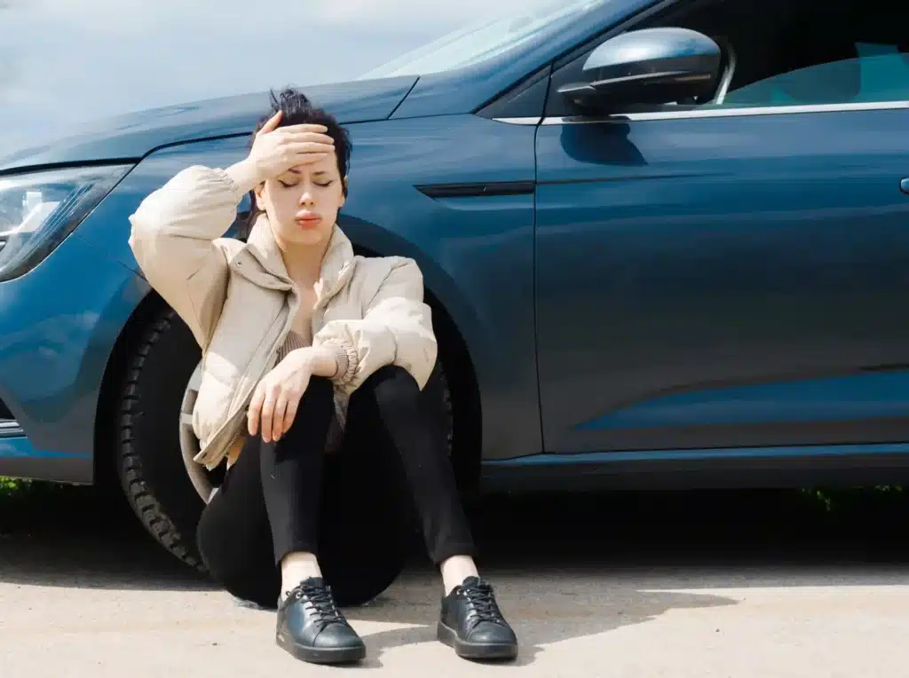 Overwelmed woman sitting up against her car