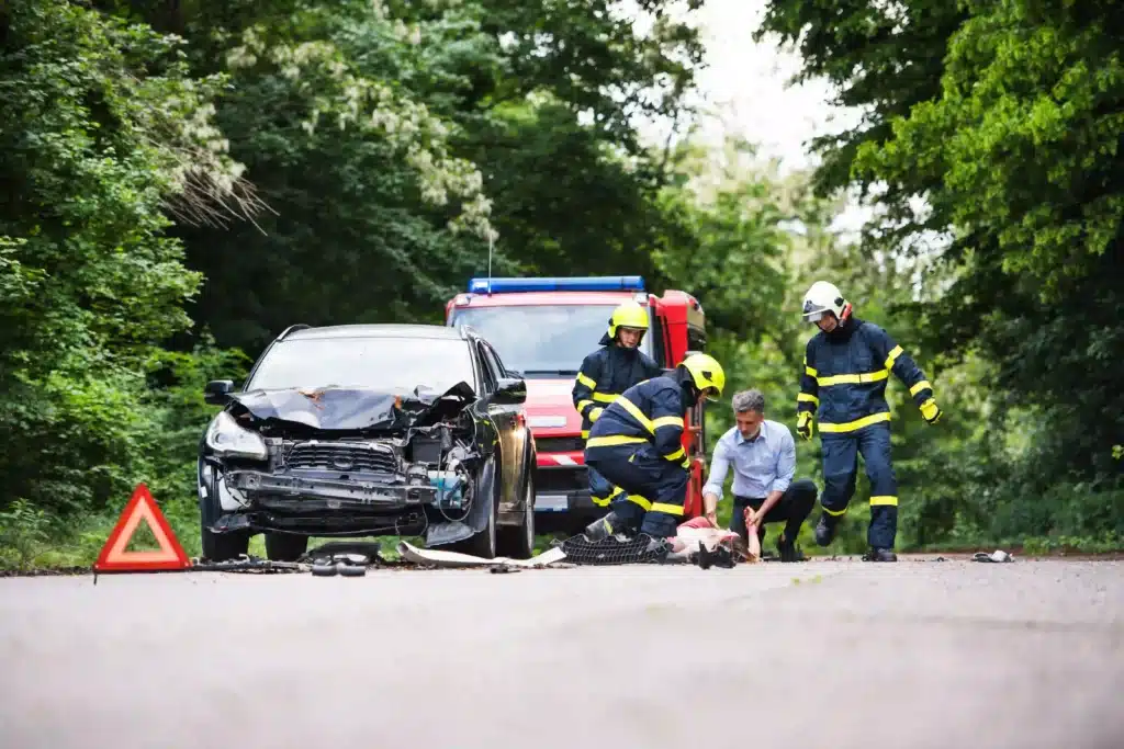 Three Firefighters Helping A Young Injured Woman Lying On The Road After An Accident.