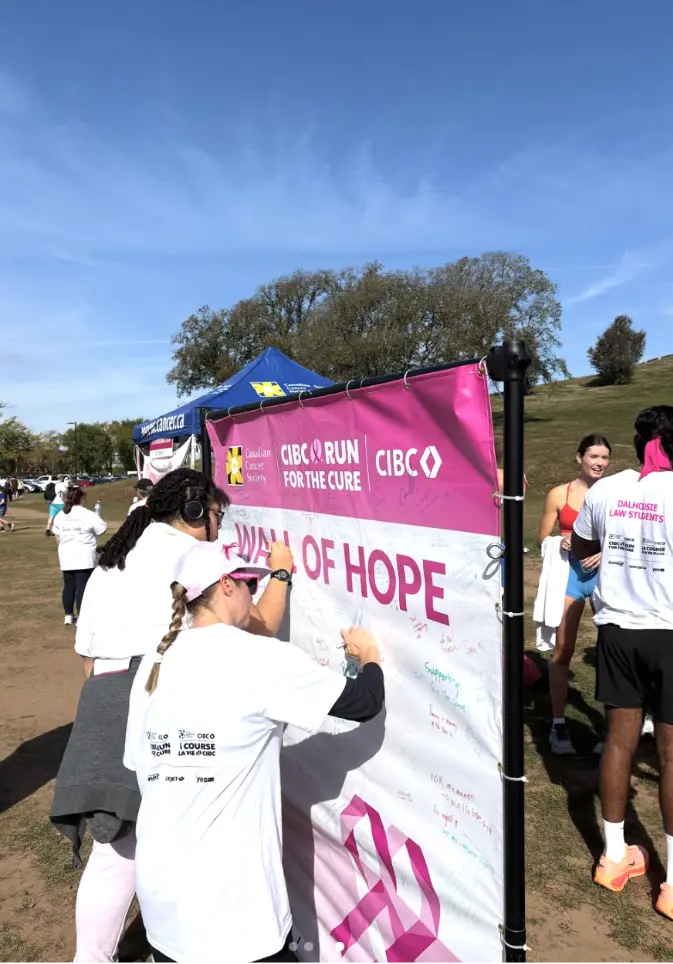 Two women writing messages on a large pink and white "Wall of Hope" banner at the CIBC Run for the Cure event
