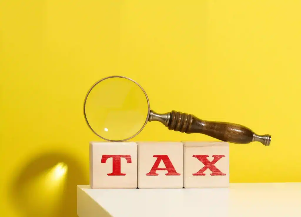 Wooden cubes with the inscription tax and a brown magnifying glass on a yellow background
